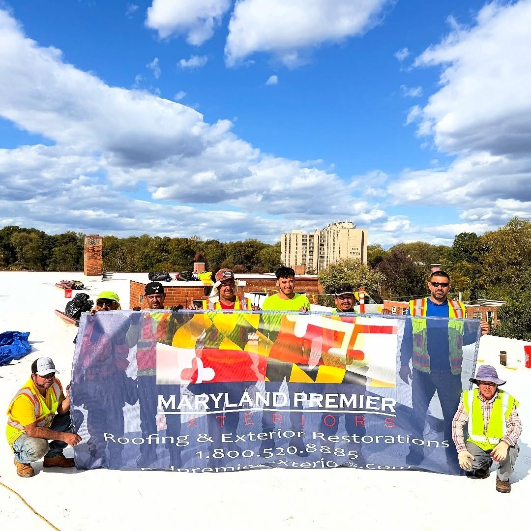 Crew standing on a white flat roof holding a large Maryland Premier Exteriors banner