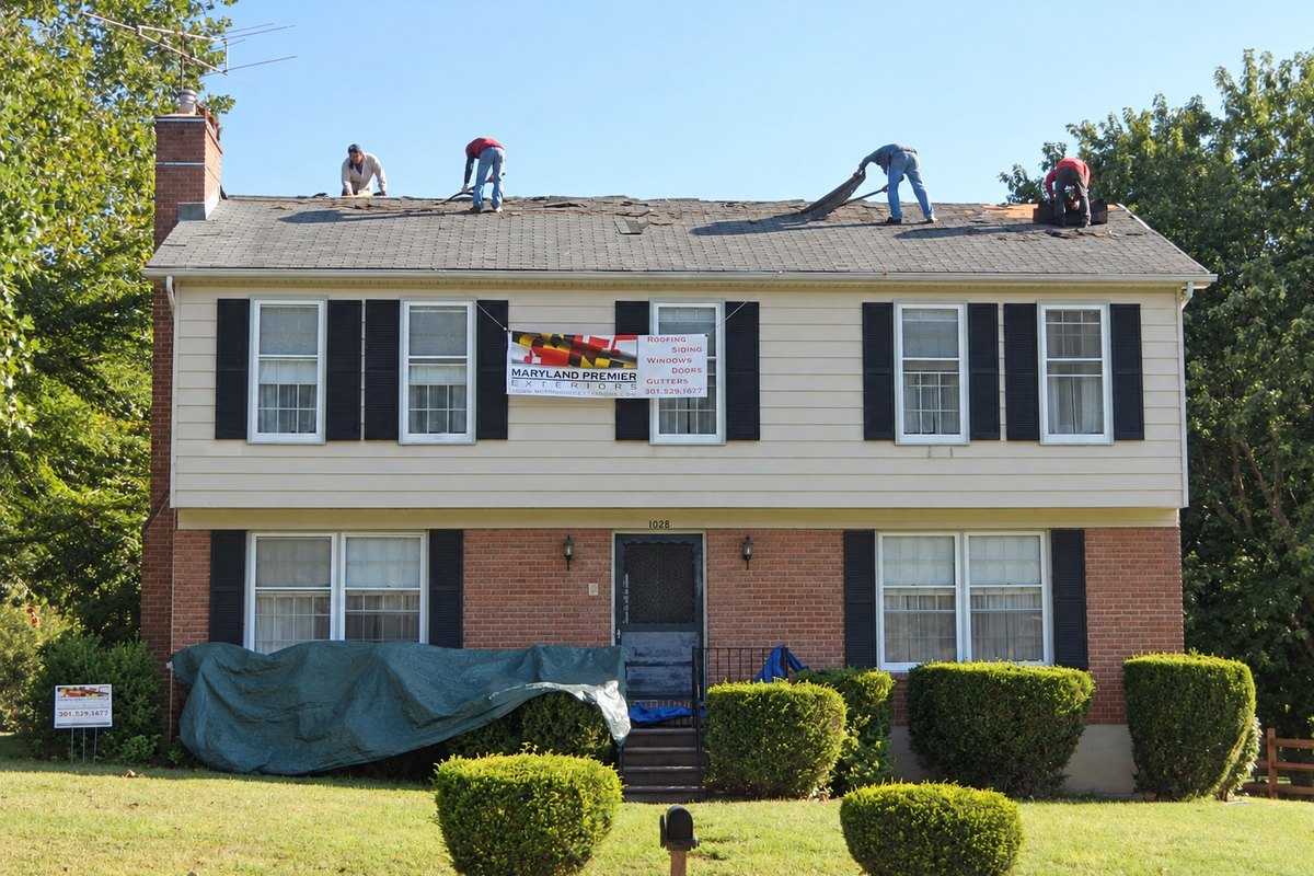 Roofers peeling old shingles off a two-story house with a company banner on the front