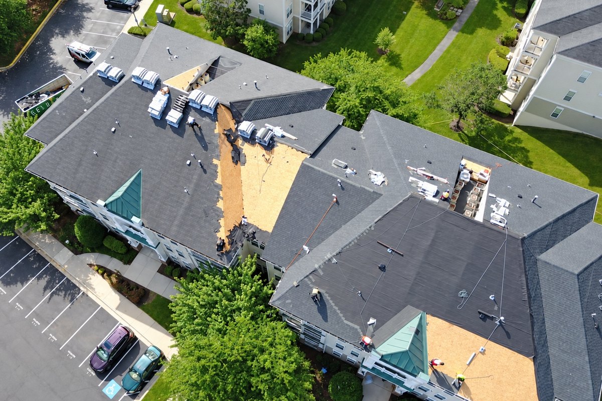 Drone view of an apartment building roof being replaced with gray shingles and exposed plywood