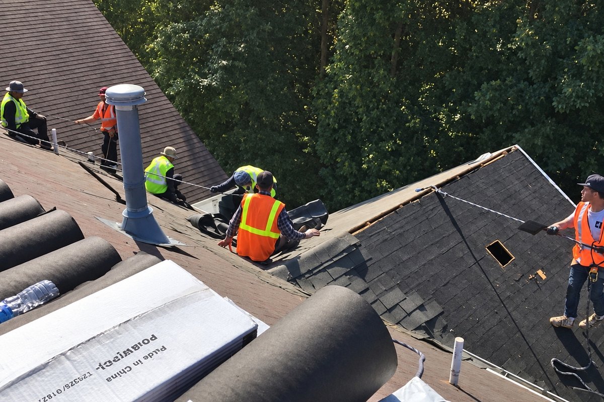 Crew of roofers working on a stripped apartment roof beside rolls of felt