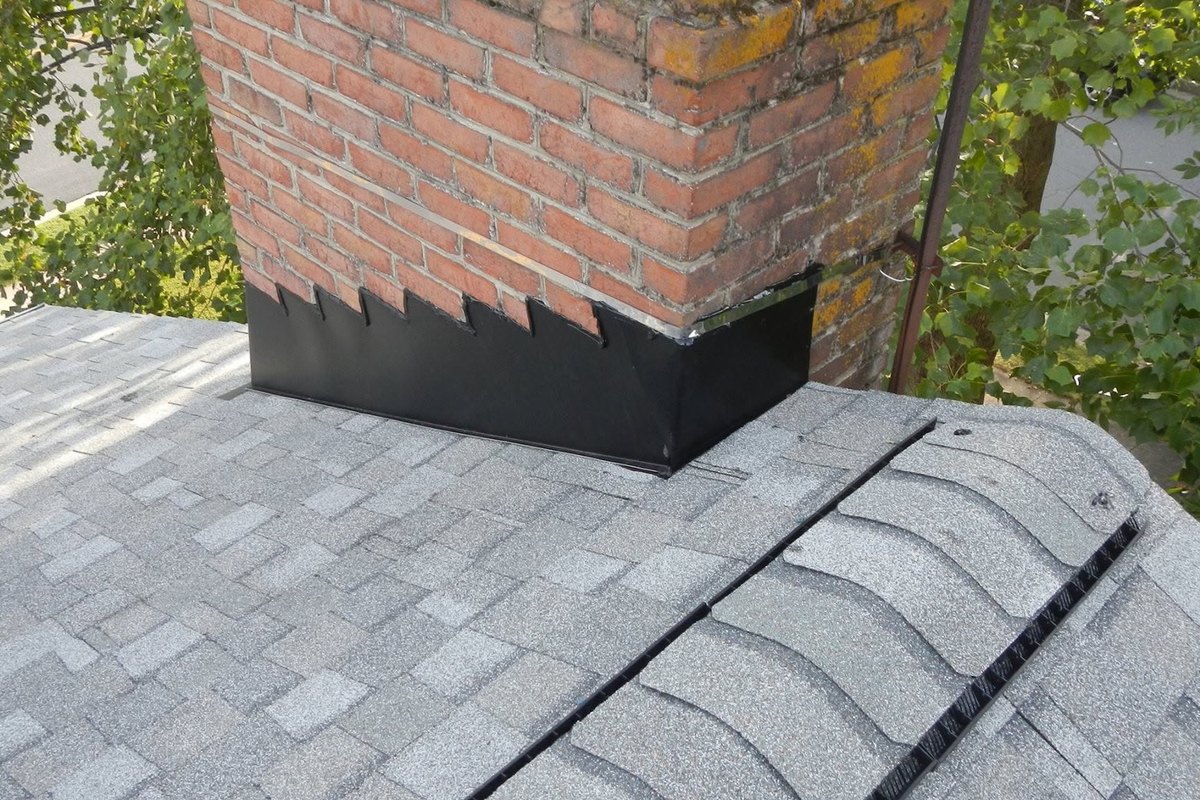 Black metal flashing around a brick chimney on a new light gray shingle roof with a ridge vent