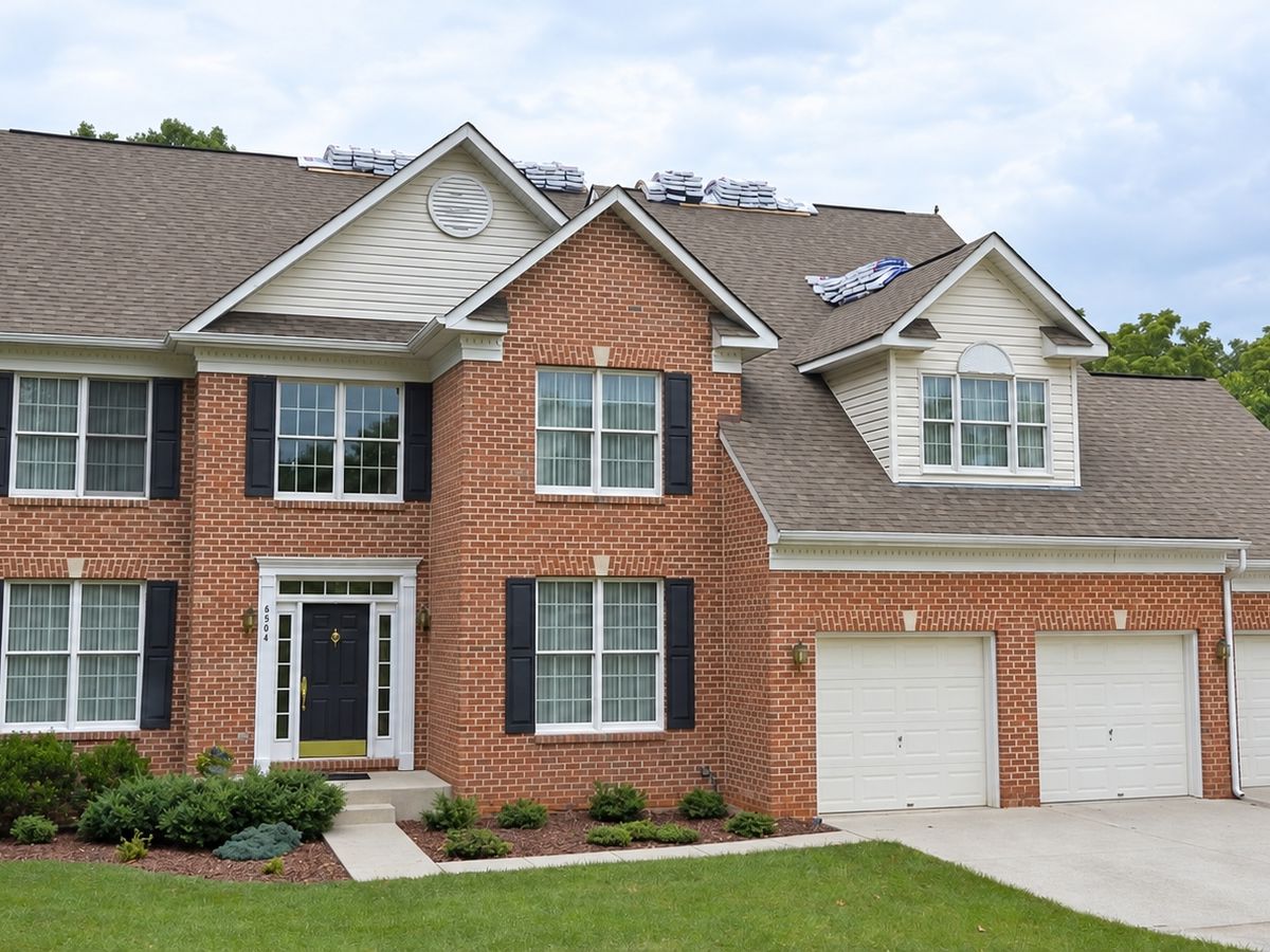 Brick house with a brown shingle roof and bundles staged along the ridges