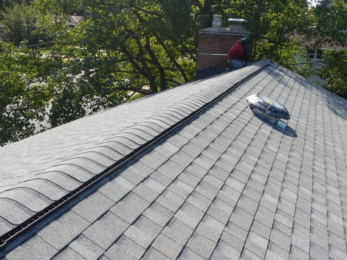 Gray shingle roof with a black ridge vent and a solar attic fan on a house with a brick chimney