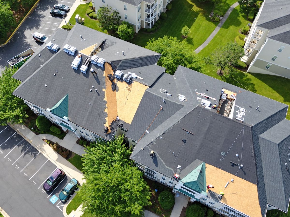 Drone view of an apartment building roof being replaced with gray shingles and exposed plywood