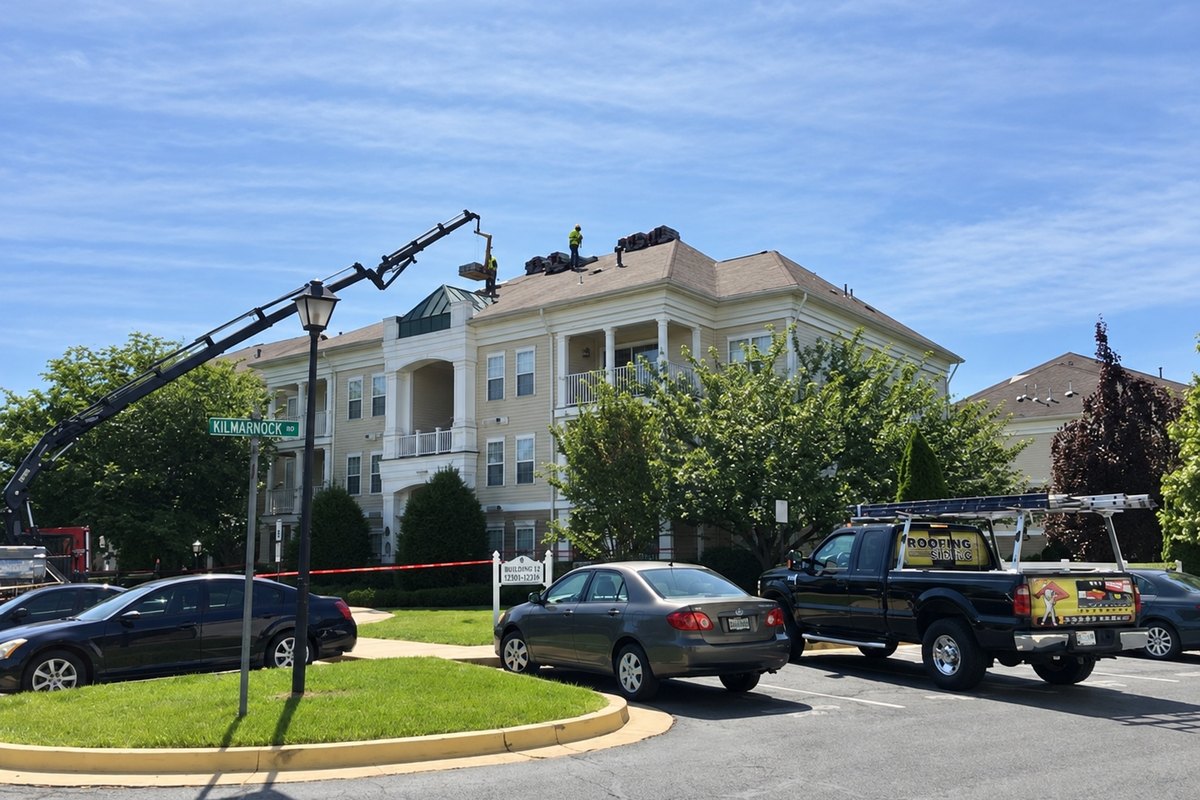 Three-story apartment building with a roofer on the ridge receiving a shingle pallet from a crane