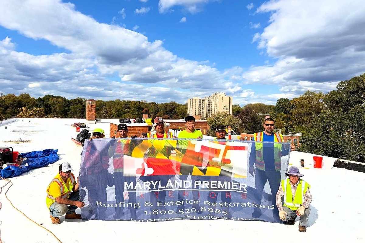 Crew standing on a white flat roof holding a large Maryland Premier Exteriors banner