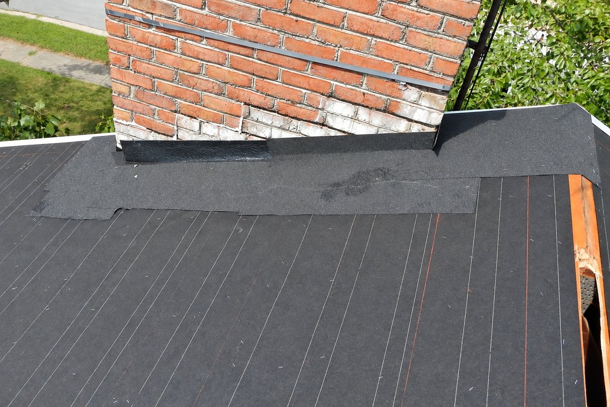 Black underlayment and flashing around the base of a brick chimney on a roof