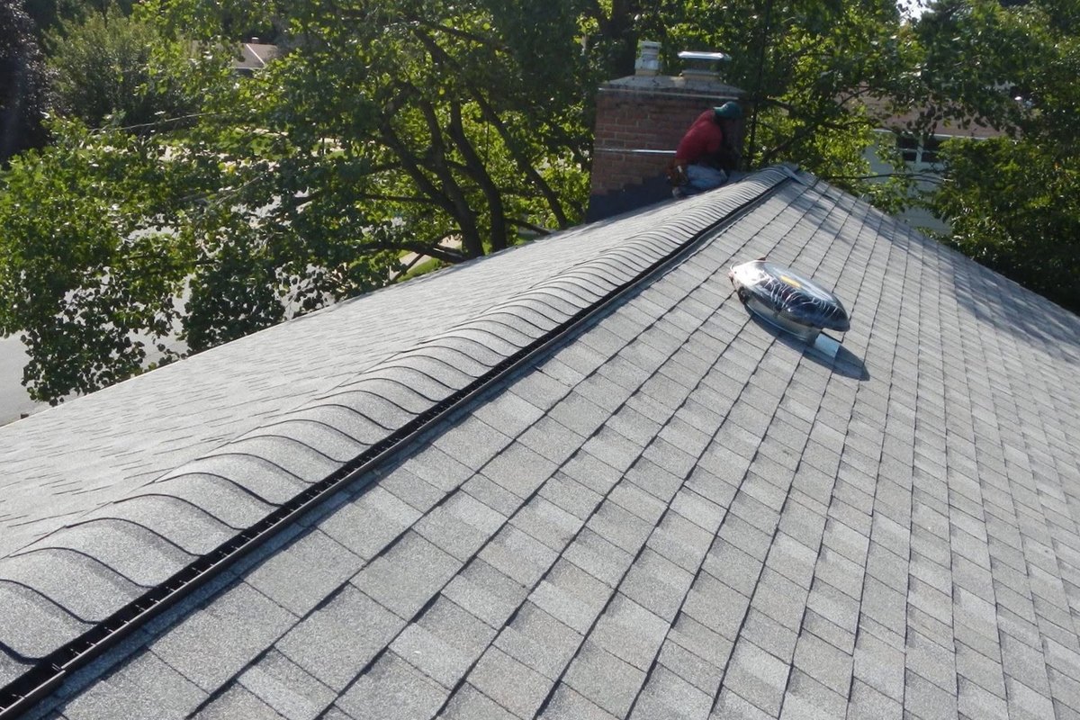 Gray shingle roof with a black ridge vent and a solar attic fan on a house with a brick chimney