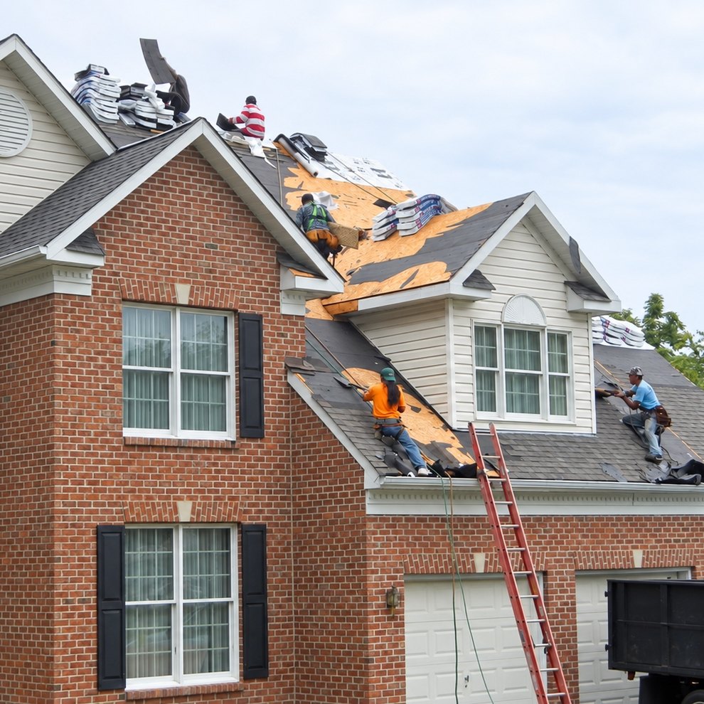 Roofers tearing off the roof of a large brick colonial with shingle bundles at the ridge