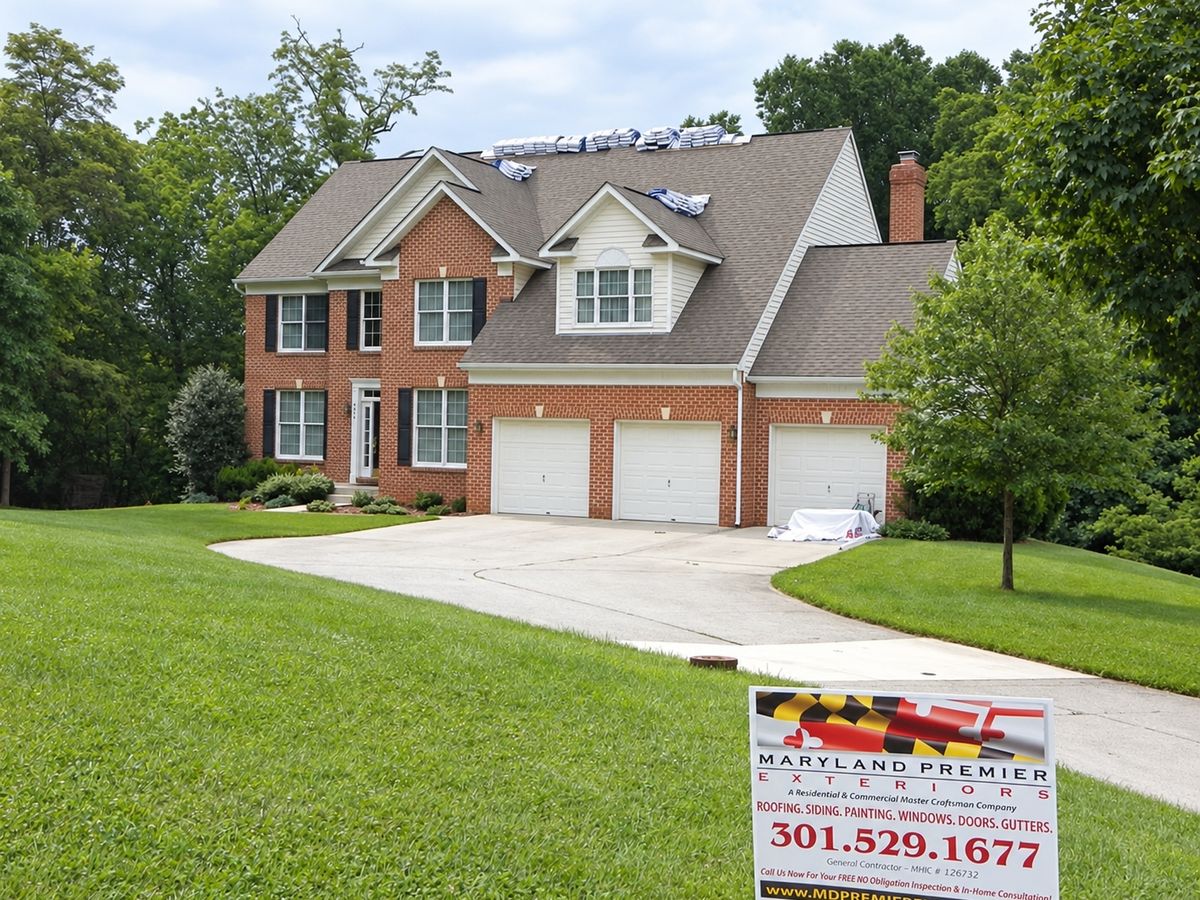 Large brick colonial with a brown shingle roof being re-roofed: white-wrapped shingle bundles staged along the ridge