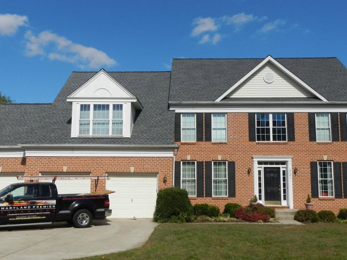 Finished brick colonial with a new gray shingle roof over several gables and a dormer, seen from the lawn