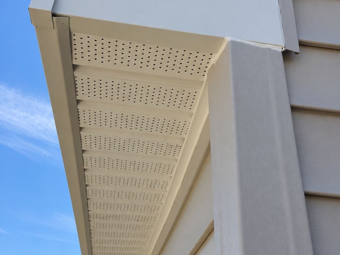 Low upward view of a house corner: white perforated vinyl soffit panels under the roof edge