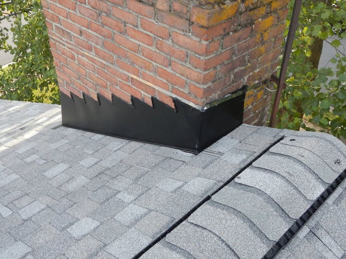 Close drone view of a light gray shingle roof around a red brick chimney