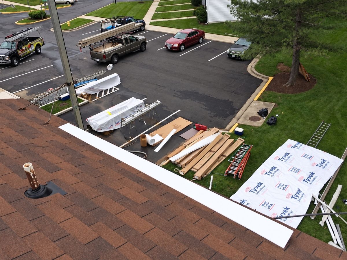 Looking down from a brown shingle roof edge with a white drip edge strip and a plumbing vent boot onto an apartment