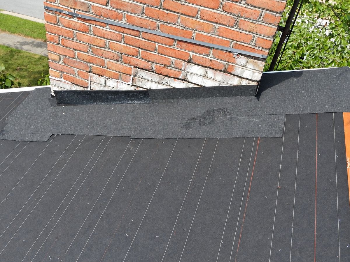 Drone view of a roof deck covered in black felt underlayment with a patched section of felt and a strip of black