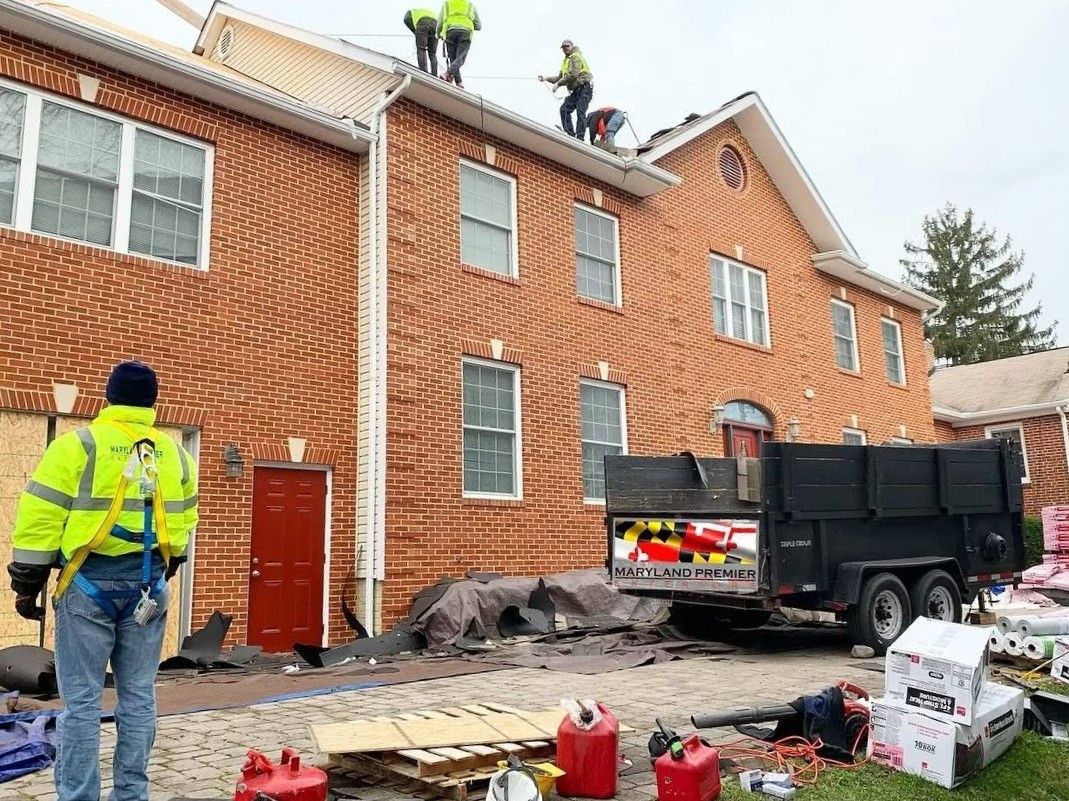 Crew of four roofers in hi-vis vests on the roof of a large two-story red brick building with white trim and a round gable