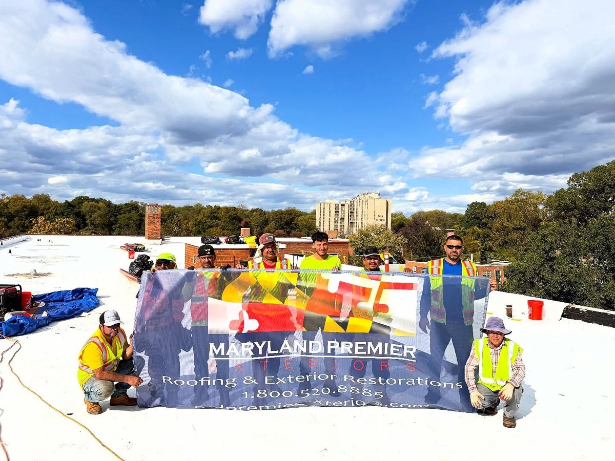 Seven crew members in yellow and green hi-vis vests and caps stand and kneel on a white flat commercial roof