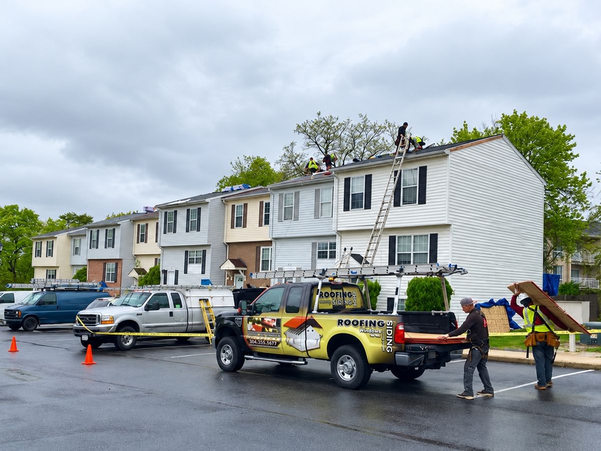 Row of townhomes in rain-gray light with roofers working on the stripped roof of the white end unit