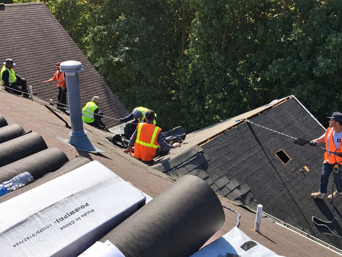 Close drone view of a crew of six roofers in hi-vis vests working on an apartment roof