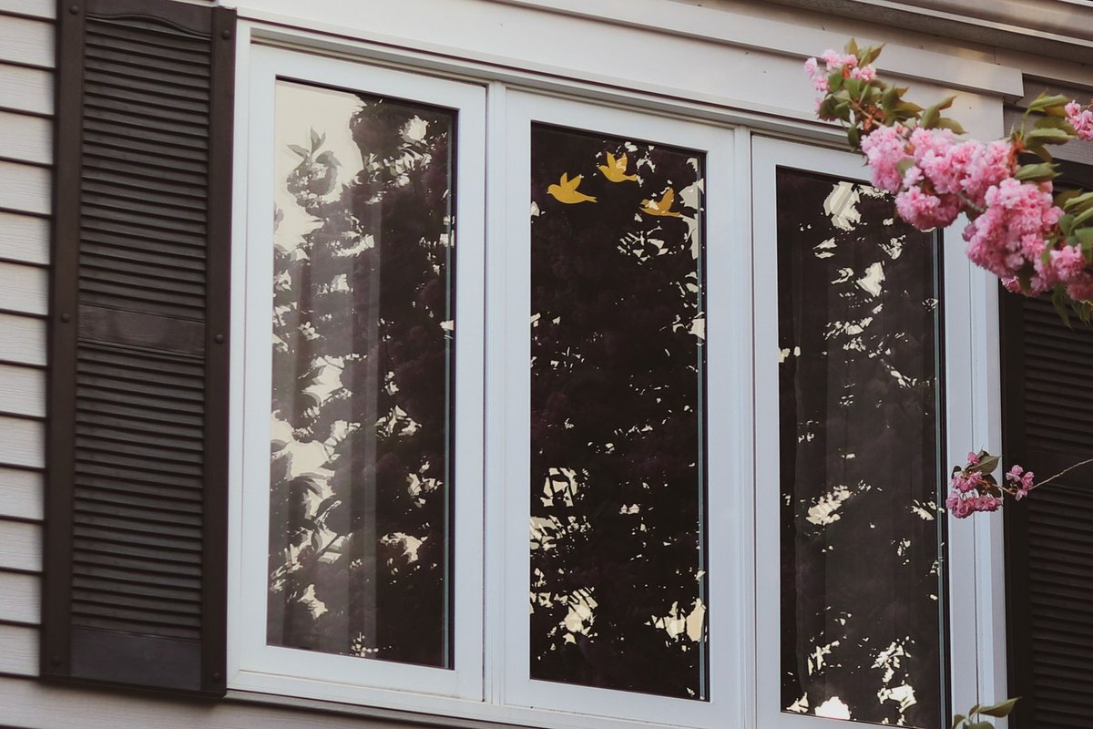 White triple casement window between black shutters on a gray vinyl-sided house
