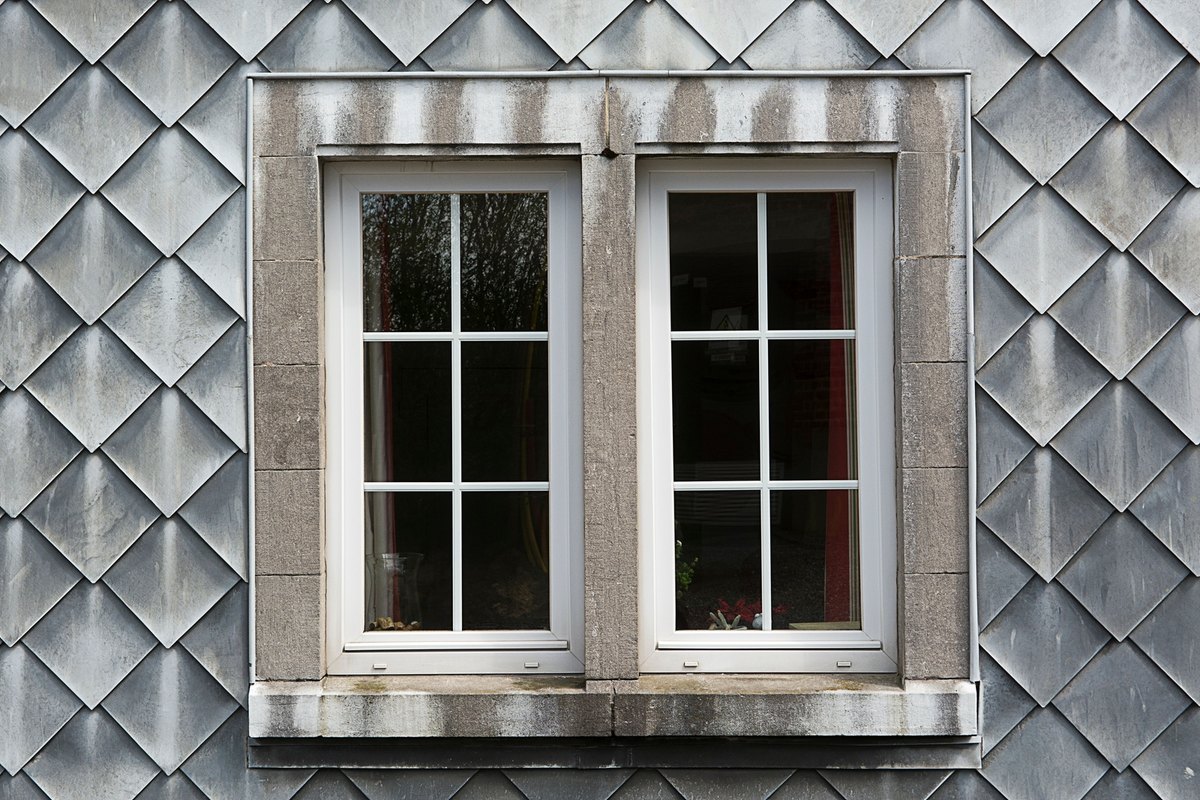 Pair of new white casement windows with grids set into a gray shingled wall