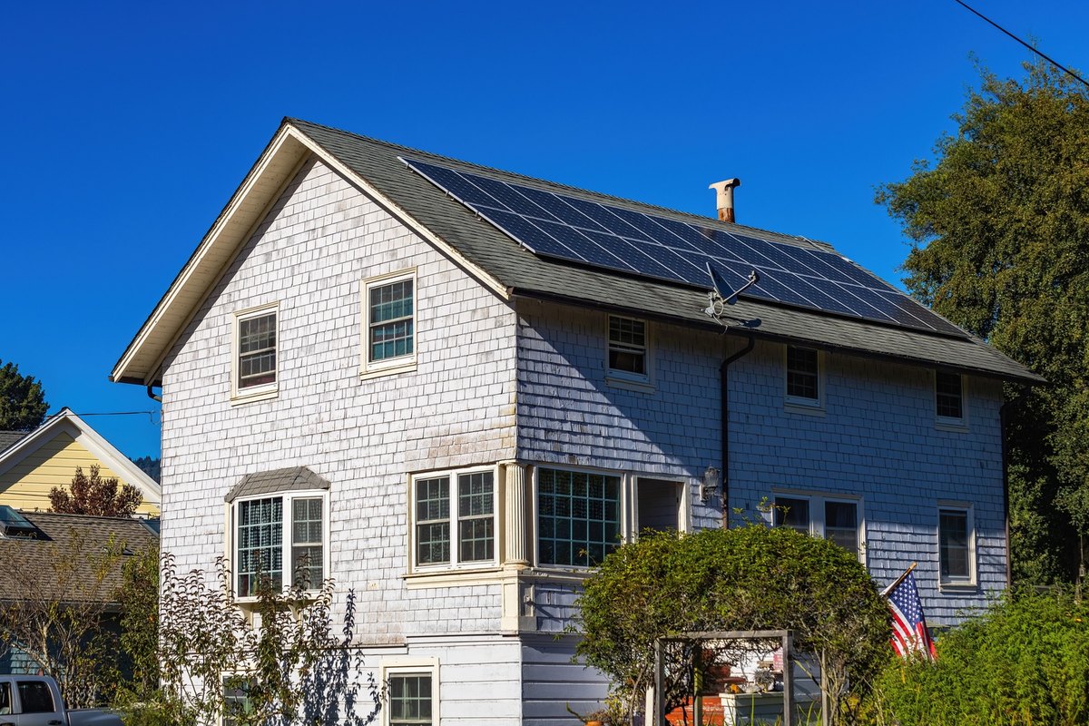 White shingle-sided house with rows of black solar panels on its gray asphalt roof