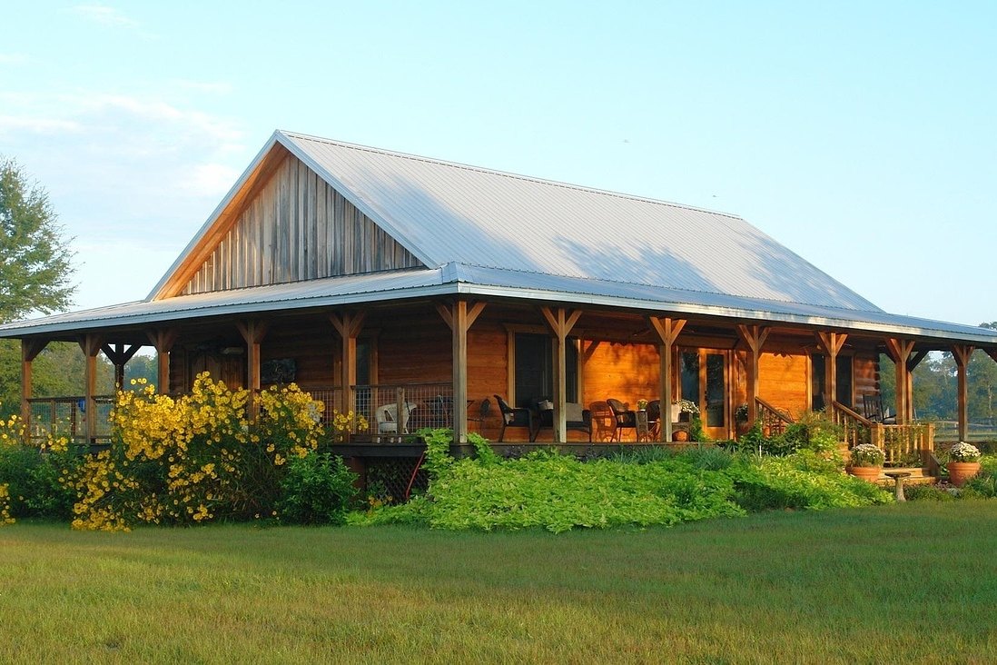 Wood-sided house with a broad silver metal roof over a deep wraparound porch