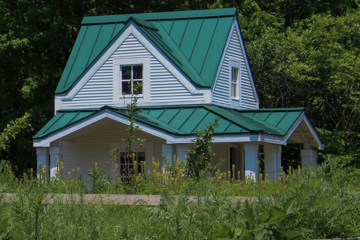 White clapboard house with a green standing seam metal roof over its gables and porch