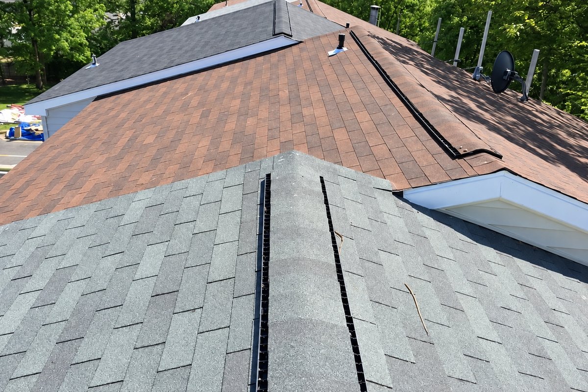 Drone view of new gray ridge cap shingles on a townhome roof next to older reddish-brown slopes