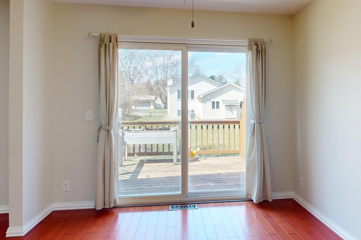 White sliding glass patio door between beige curtains opening onto a wooden deck