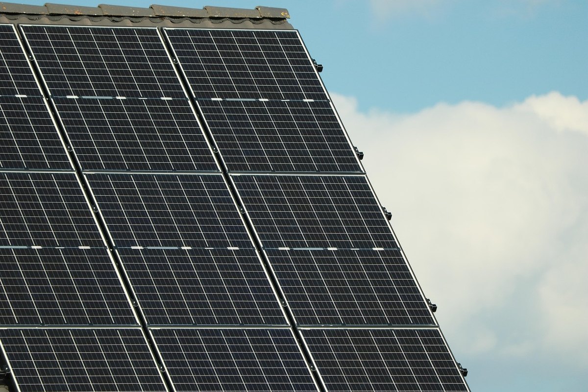 Rows of black solar panels mounted on a pitched roof against a blue sky