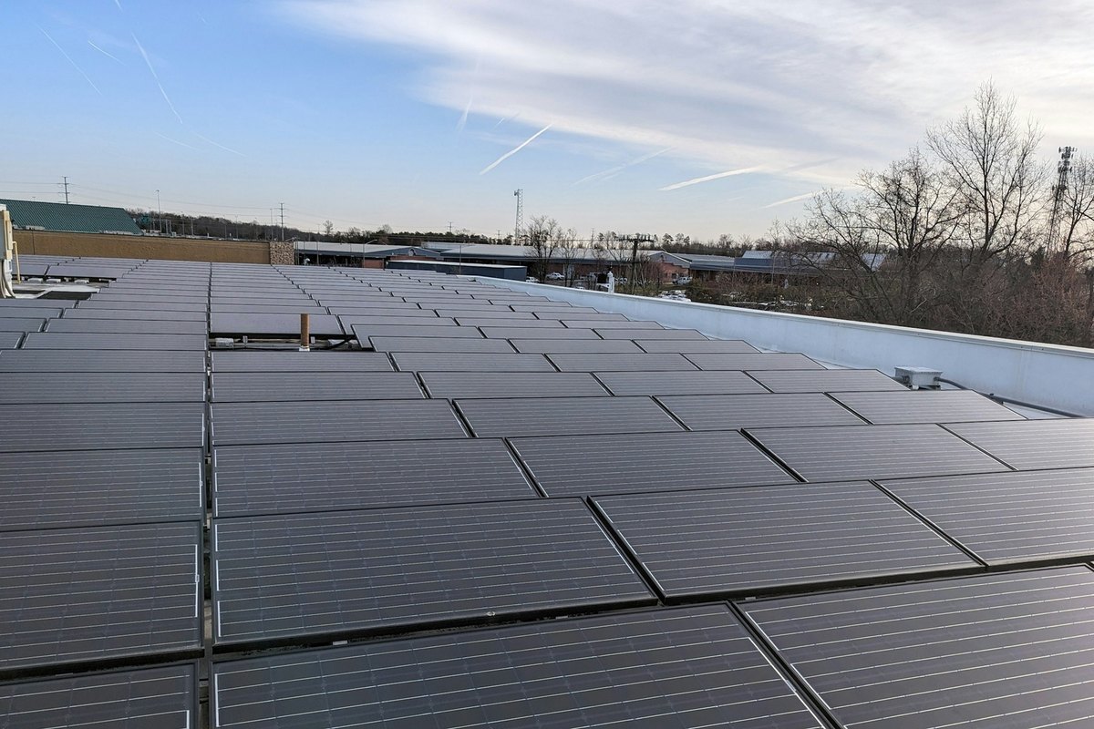 Large flat commercial roof covered in rows of solar panels with a white parapet edge