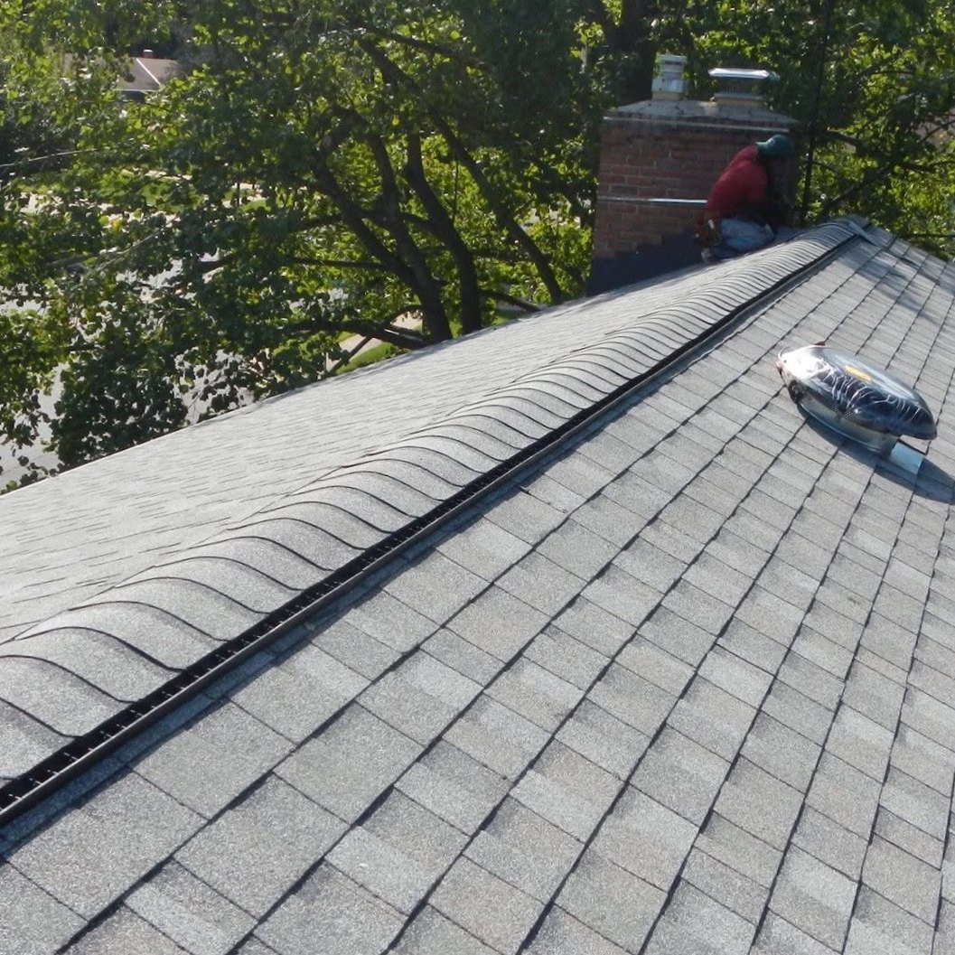 Gray shingle roof with a black ridge vent and a solar attic fan on a house with a brick chimney
