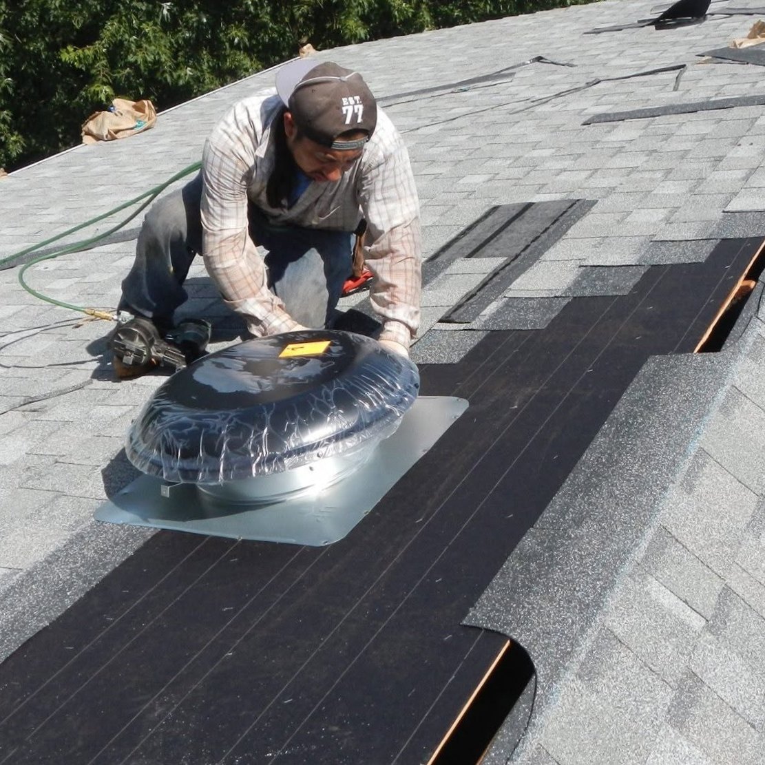 Roofer installing a solar attic fan on a gray shingle roof
