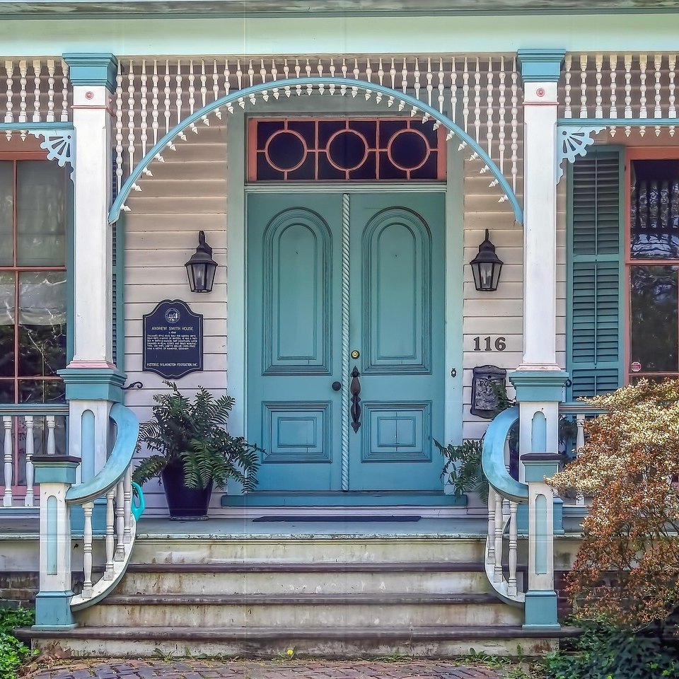 Teal double front doors under a round-window transom on the porch of a white Victorian house