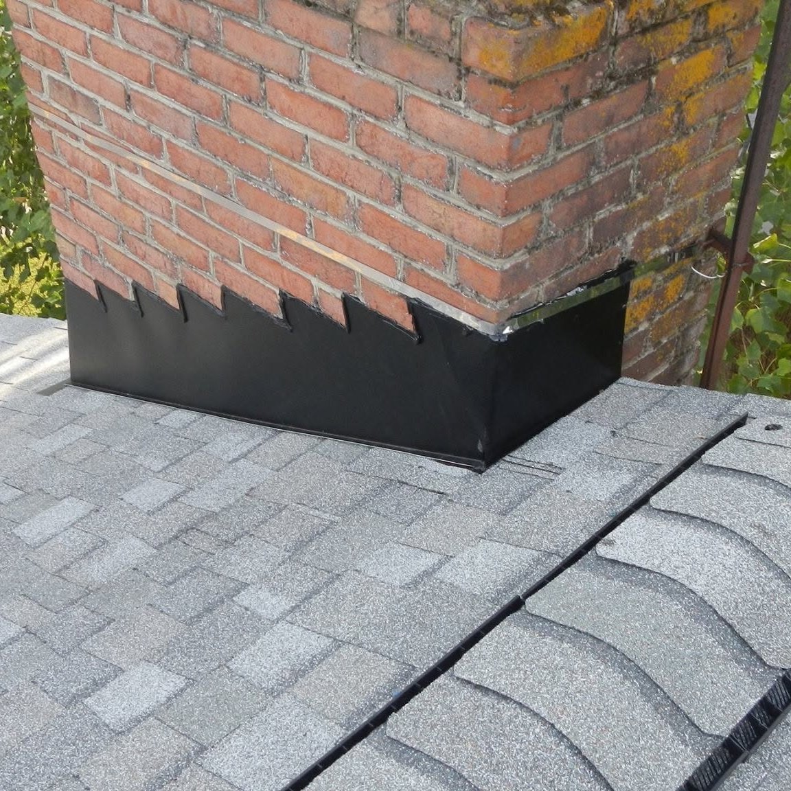 Light gray shingles and new flashing around a red brick chimney, seen from above