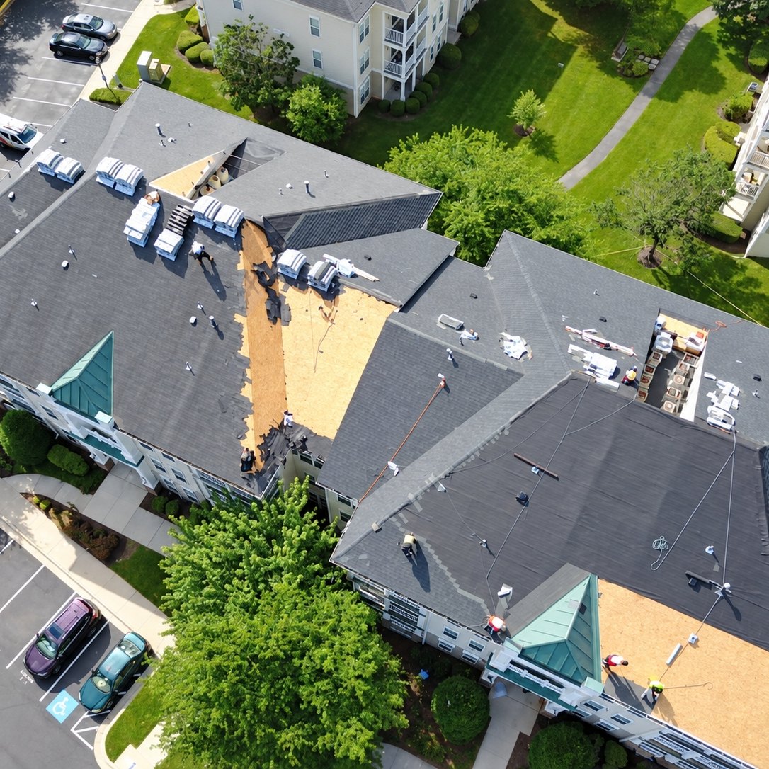 Drone view of an apartment building roof being replaced with gray shingles and exposed plywood