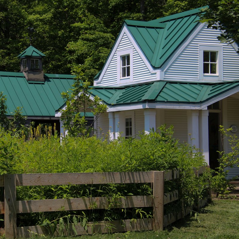 White house and outbuilding with green metal roofs and a cupola behind a split-rail fence