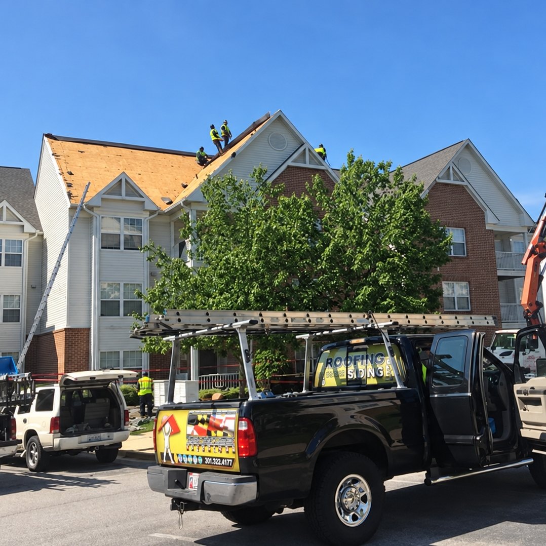Roofers on an apartment building roof stripped to plywood with a crane lifting shingles