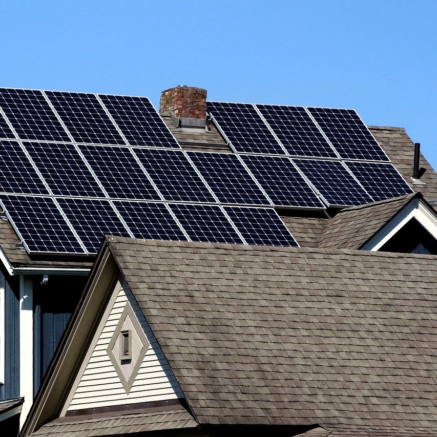 Black solar panels covering the shingle roof of a navy blue house with a brick chimney